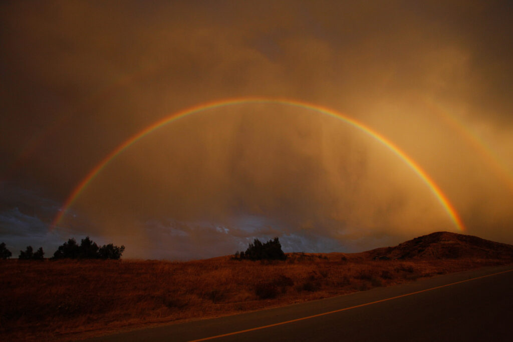 Double rainbow over rural road at sunset