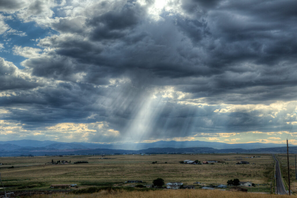 Dramatic clouds with sunrays over open landscape.