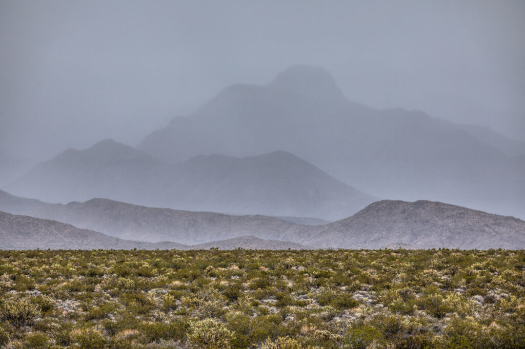 Misty mountains and desert landscape under gray sky.